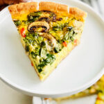 A hand holding a plate with a slice of vegan quiche on it.