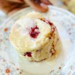 Hand holding a plate with a glazed vegan strawberry biscuits on top.