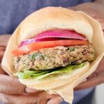 Hands holding a black bean burger wrapped in parchment paper.